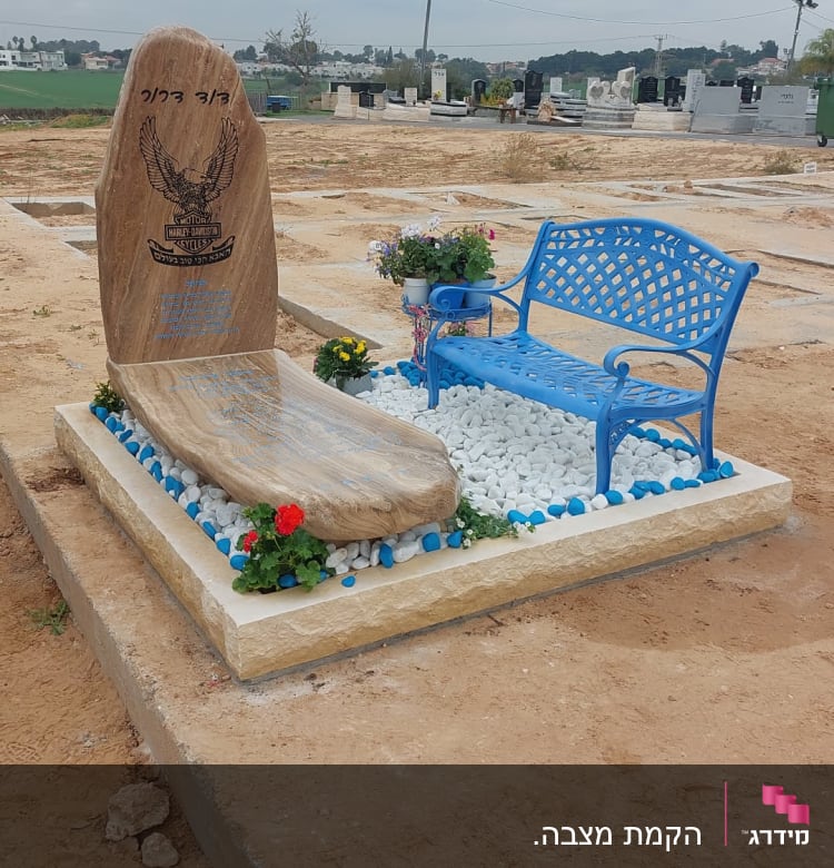 מצבה עם אבן גדולה, ספסל כחול ופרחים